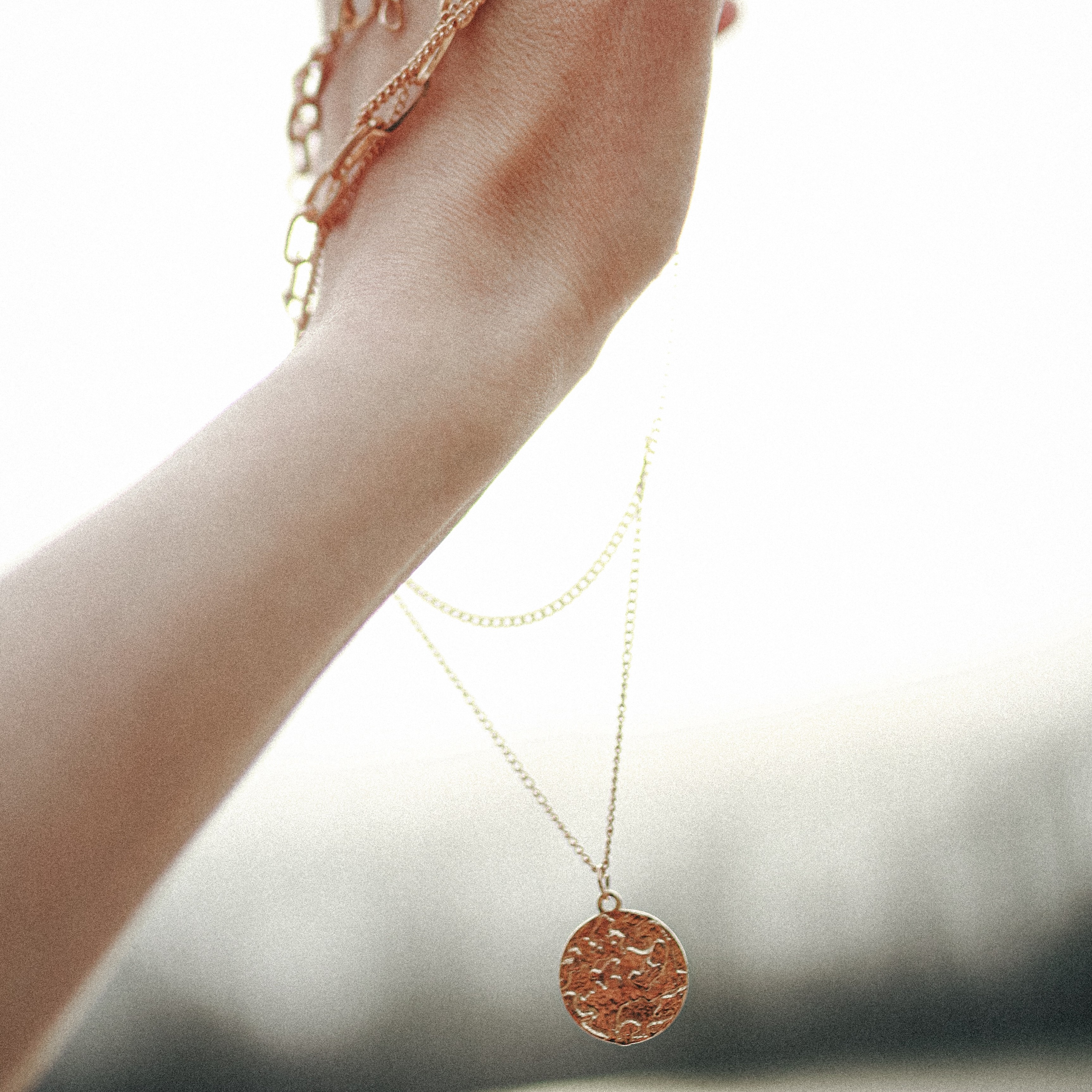 A round, gold necklace with a thin, long chain