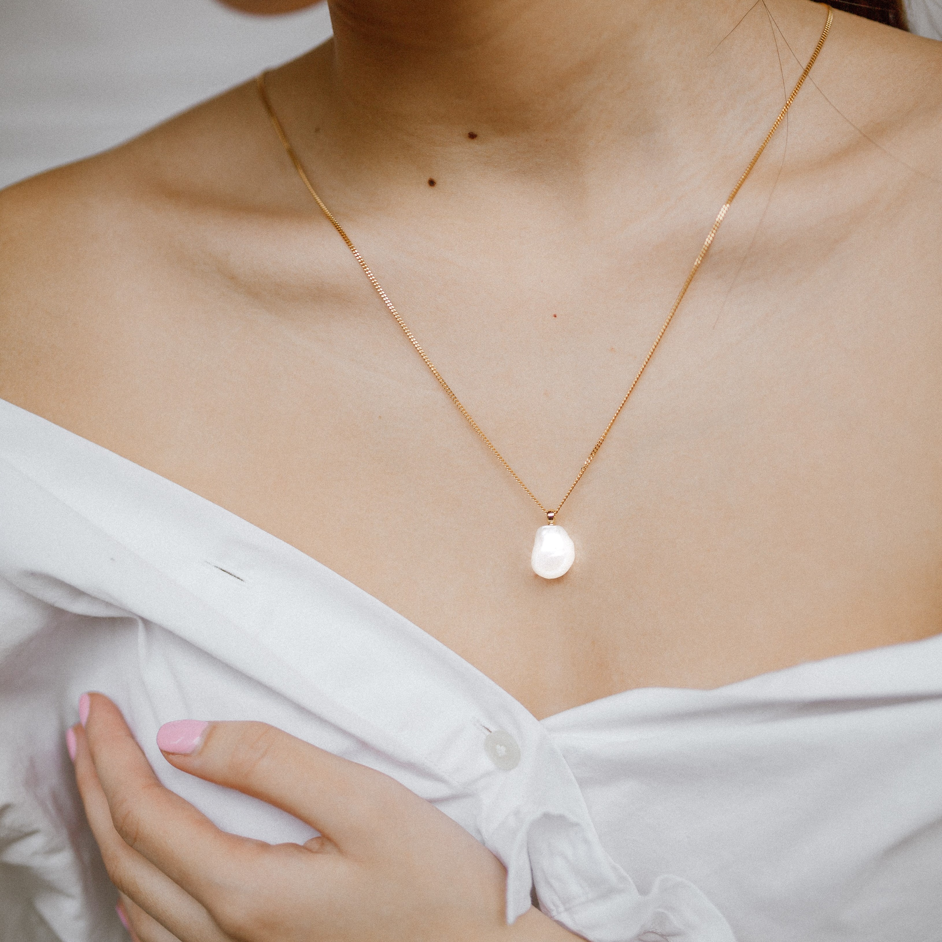 A necklace with a thin,gold chain and a shining white/pearl mineral