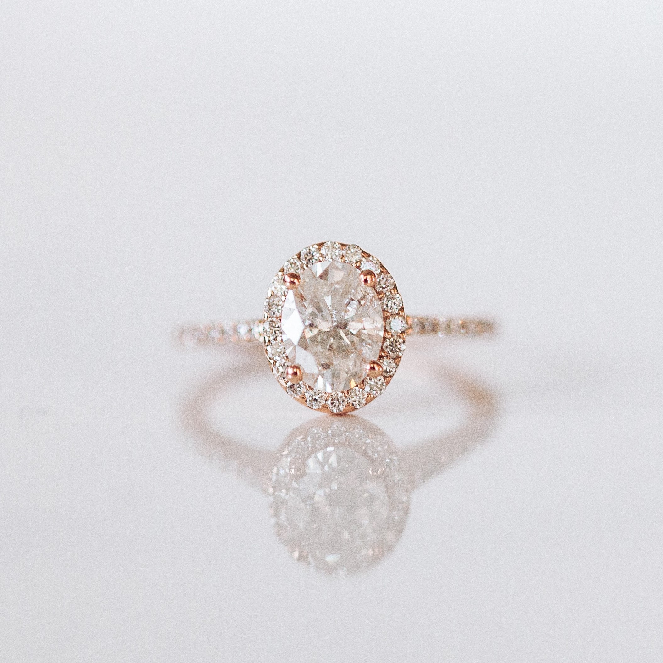 A oval rose gold diamond ring with multiple small diamonds around and one big main diamond
