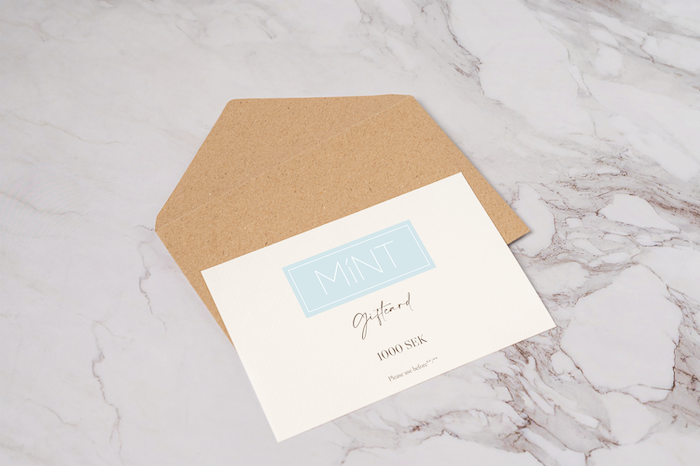 White giftcard laying on a cardboard envelope. Giftcard and envelope are laying on a white marble background.