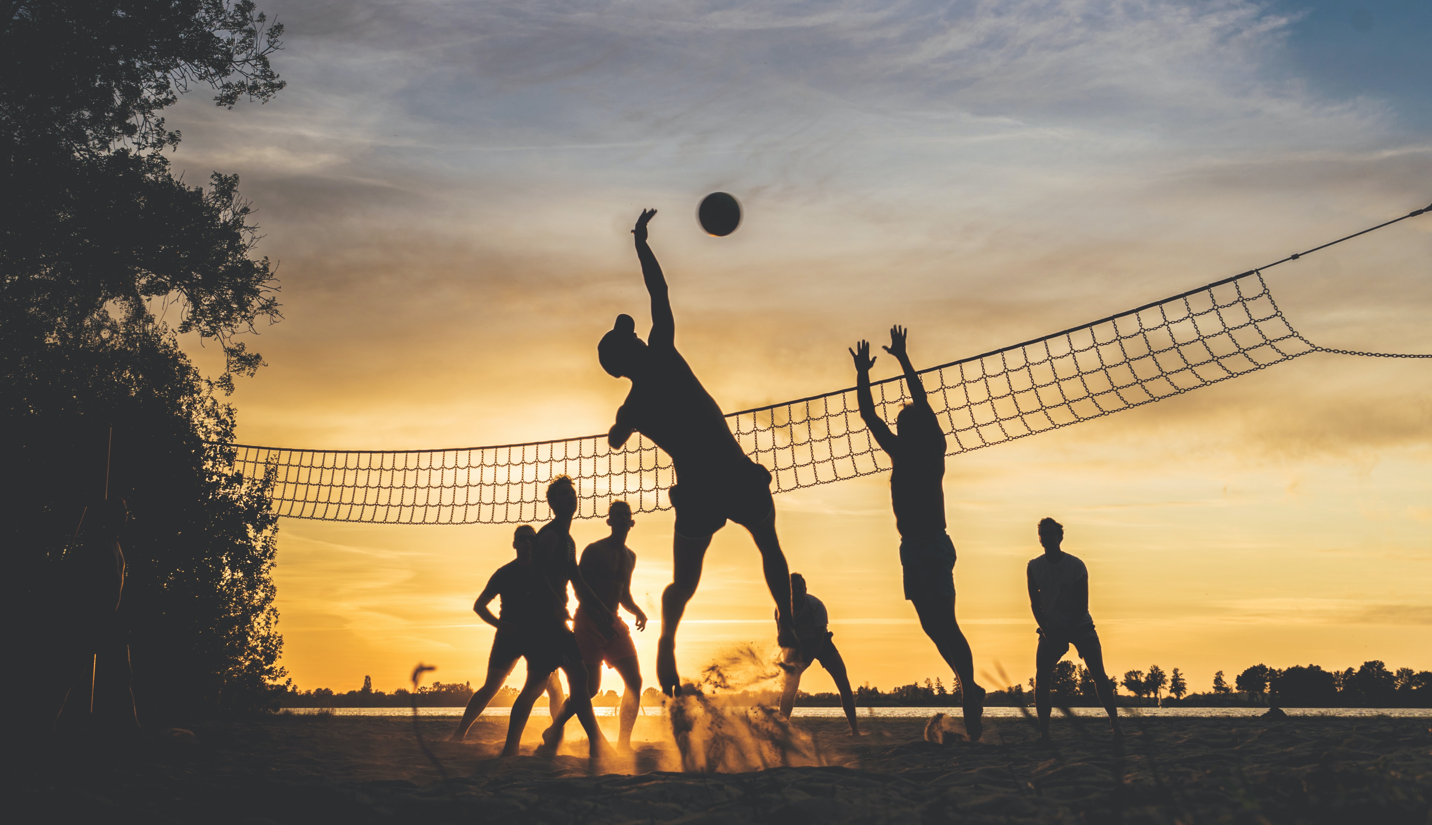 people playing volleyball in the sand during sunset